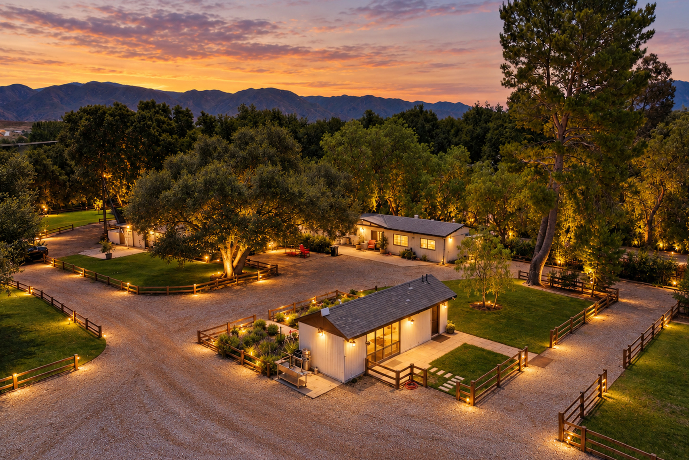 Aerial view at dusk of the gated Sand Canyon ranch, with the main home, drive and oak trees lit against the sunset and mountains