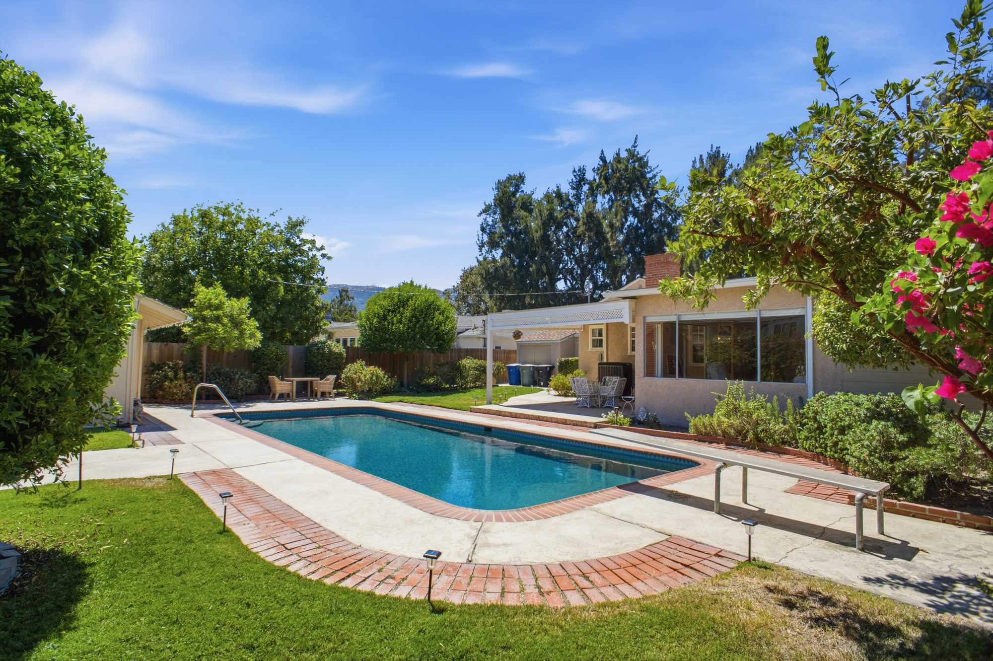 The rear yard with a rectangular pool, brick coping, covered patio and mature trees